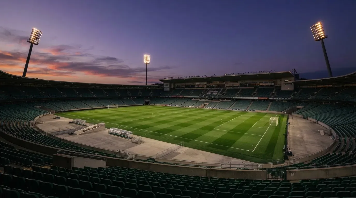 An empty football stadium with floodlight masts at dusk