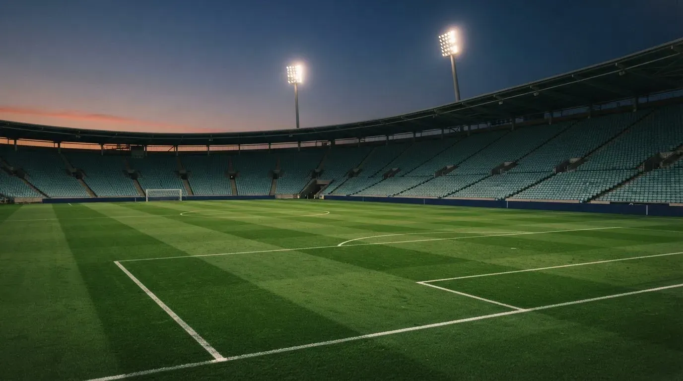 An empty football stadium with floodlight masts at dusk