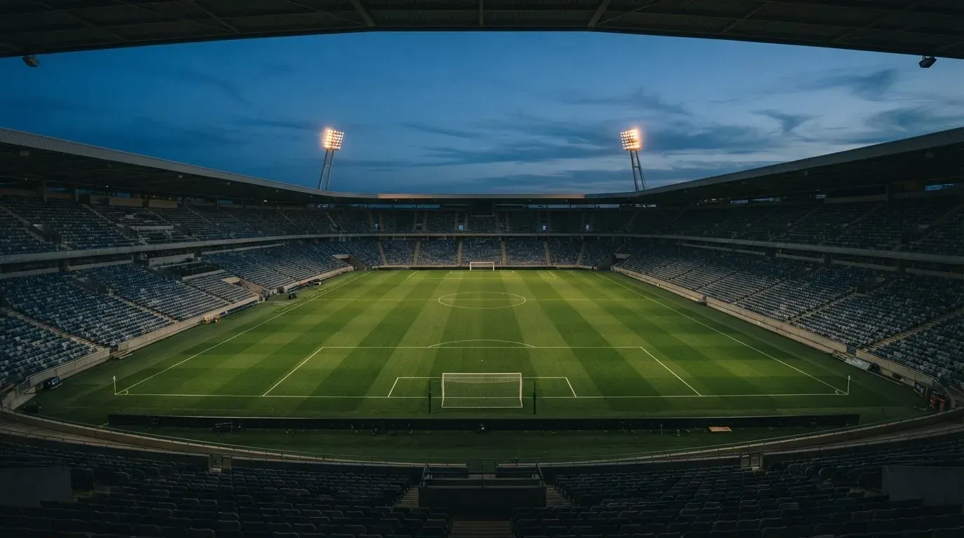 An empty football stadium with floodlight masts at dusk