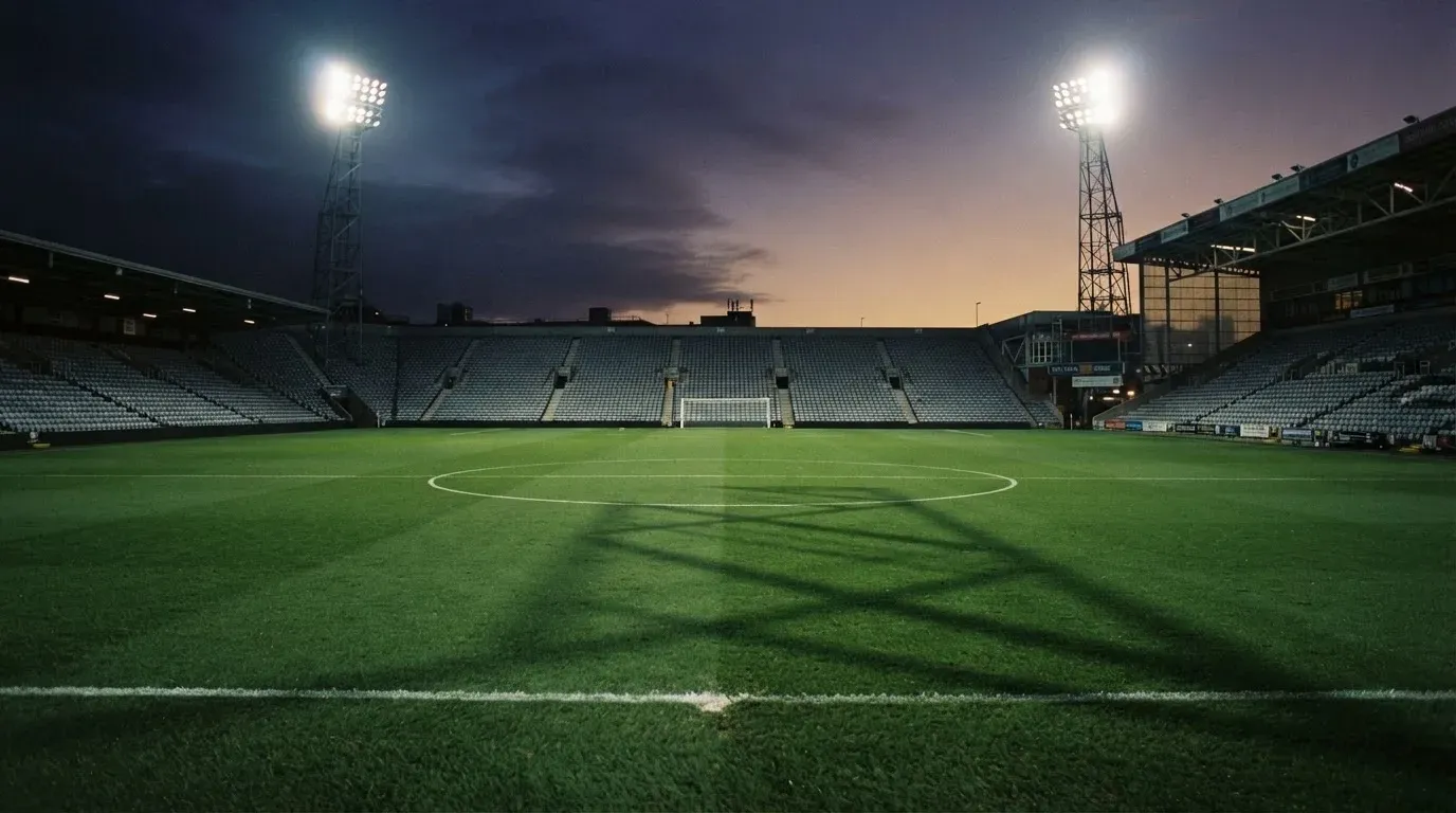 An empty football stadium with floodlight masts at dusk